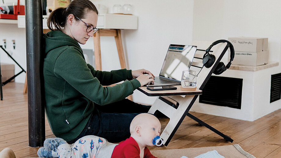 Multitasking beim Homeoffice: Mutter am Computer, daneben ein Baby auf dem Fußboden