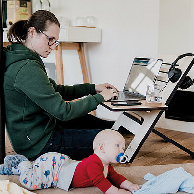 Multitasking beim Homeoffice: Mutter am Computer, daneben ein Baby auf dem Fußboden