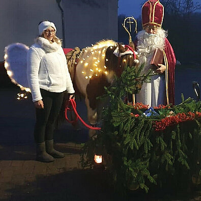 Frau als Engel mit Lichterkette, Pferd mit Lichterkette und ein Nikolaus draußen im Rahmen der Nikolausfeierlichkeiten der Kolpingsfamilie Obererbach